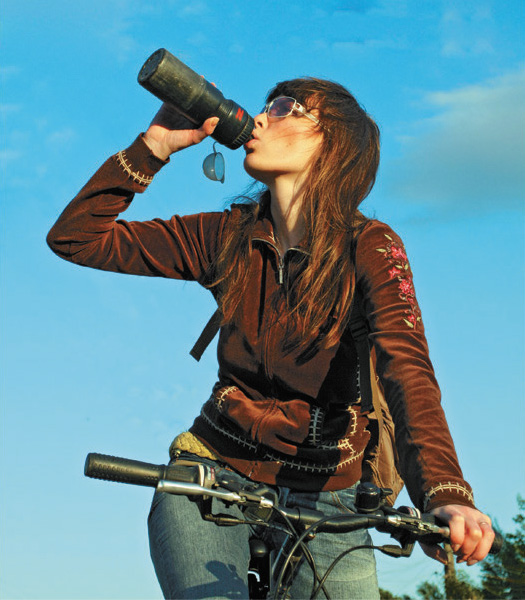 A photograph of a woman sitting on a bicycle taking a drink from a water bottle