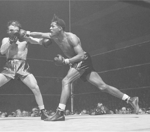 A black and white photo shows a boxing match, with one of the boxers punching the other in the face.