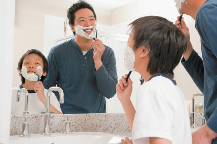A photograph shows a young boy and his father in the bathroom. Both have shaving cream on their face, and the boy is holding his razor in the same position that the father is holding his.