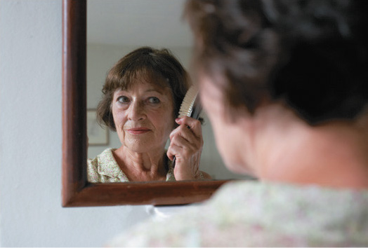 A photo of a woman looking in the mirror and brushing her hair